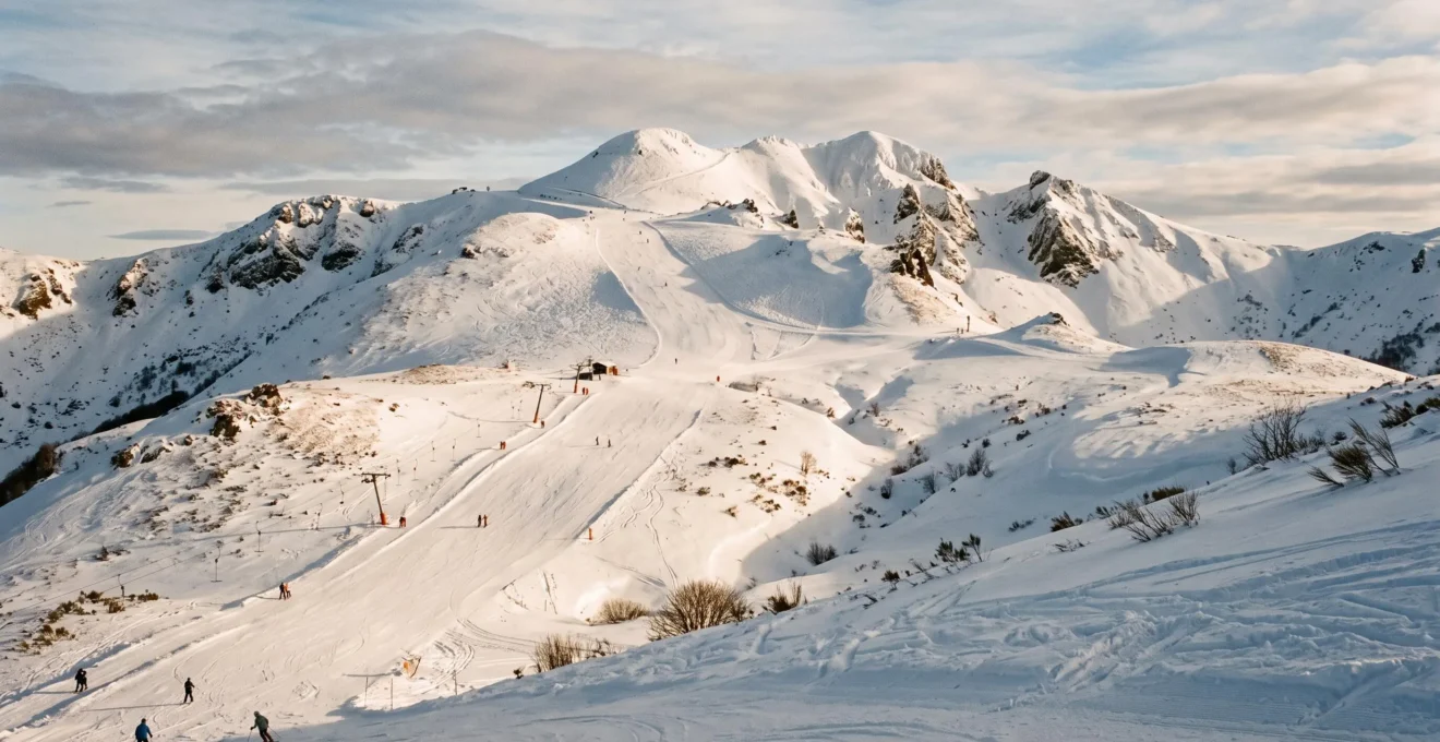 Pistes de ski enneigées du Massif Central au pied du Puy de Sancy, avec un téléski et quelques skieurs.